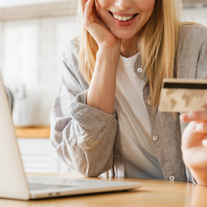Smiling woman holding a credit card near a laptop, suggesting online shopping or payment.