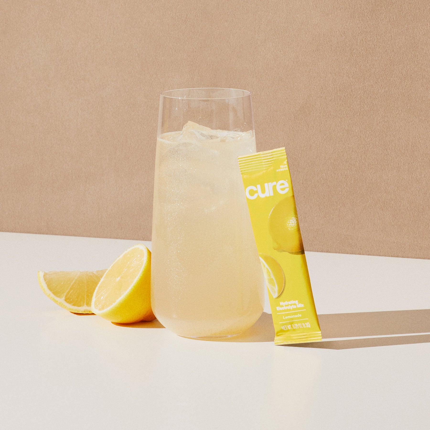 Glass of lemonade with ice, lemon wedge, and yellow packet labeled 'cure'