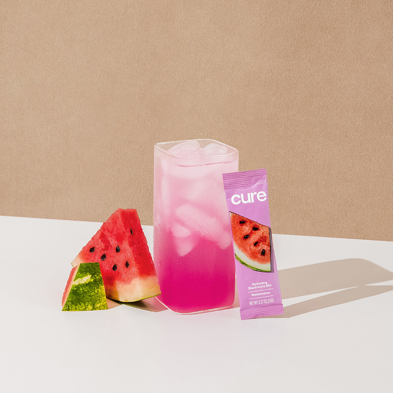 Pink iced drink next to watermelon slices and a purple packet labeled 'cure' with watermelon image