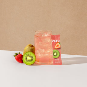Glass of pink drink with ice, strawberry, kiwi, and 'cure' packet showing strawberry and kiwi images